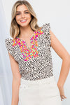 Woman wearing Peyton embroidered cheetah print blouse in cream with ruffle cap sleeves and vibrant design.