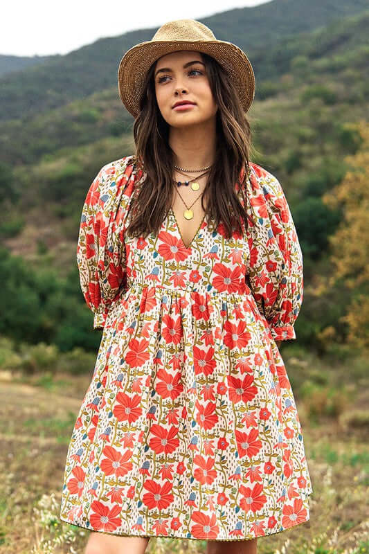 In the Meadow Floral Mini Dress in Coral and Cream on a model, featuring a V-neck and puff sleeves, perfect for warm days.