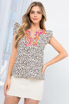 Woman wearing Peyton embroidered cheetah print blouse in cream with ruffle cap sleeves and vibrant design.