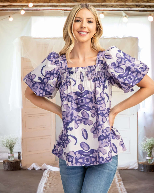 Model wearing a purple floral print puff sleeve top, showcasing its smocked detail and flattering A-line fit.