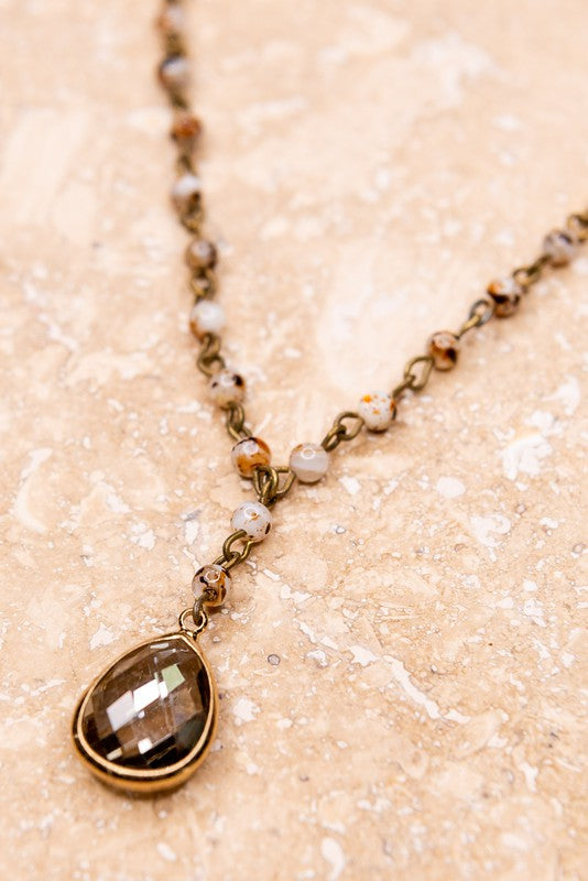 Close up of Frannie White Quail Natural Stone Bead Necklace with teardrop brown crystal charm and bronze chain.