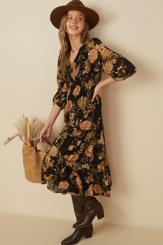 Hannah floral print smocked dress in black, featuring a V-neckline and tiered skirt, styled with a hat and tote.