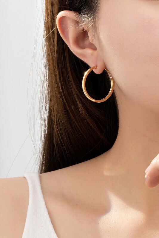Close-up of a woman wearing polished gold hinged hoop earrings, showcasing elegance and versatile style.